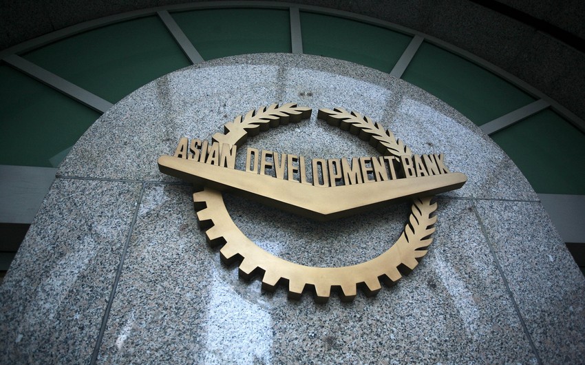 "Asiya İnkişaf Bankının loqosu daş üzərində — qızılı rəngli dişli dairə və dəfnə yarpaqları ilə bəzədilmiş emblem, ortasında 'ASIAN DEVELOPMENT BANK